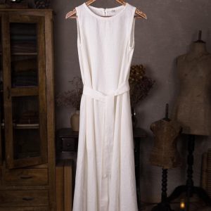 One white linen dress on a wooden hanger, front view, sleeveless with a round neckline and a long loose skirt with a tie belt at the waist.