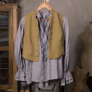 Gray linen blouse under an olive button-front vest, displayed on a wooden hanger in a front full-length crop, with puffed long sleeves, ruffled cuffs, center gathers, lower hem, and studio backdrop.