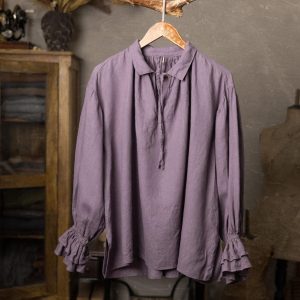 Dusty purple linen blouse shown from the front on a wooden hanger, with a small pointed collar, split neckline, narrow neck tie, dropped shoulders, long loose sleeves, gathered wrists, and double ruffled cuffs.